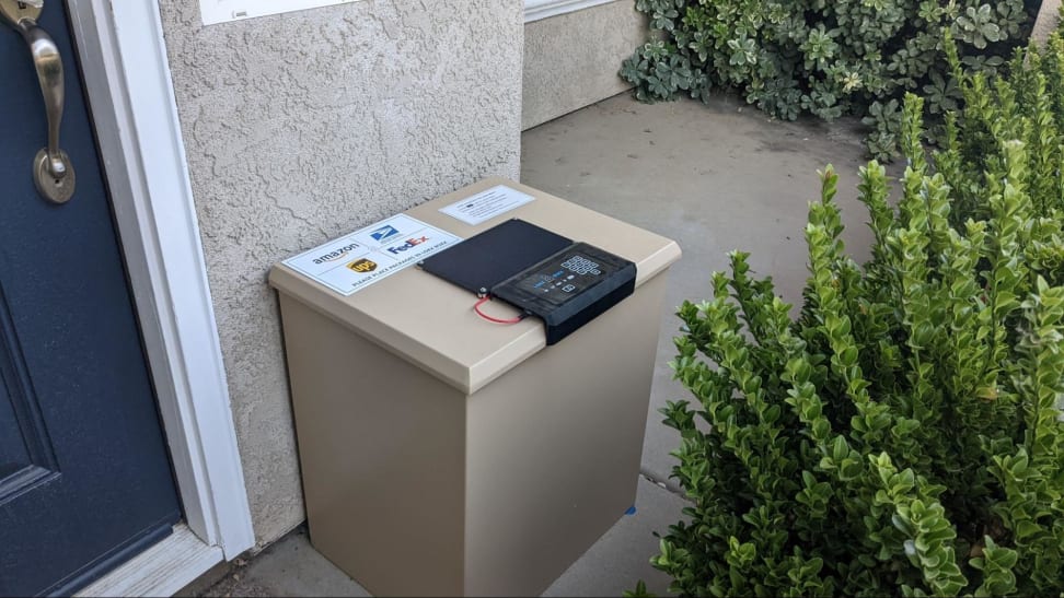 The Loxx Boxx sits outside next to an exterior door and a bush.