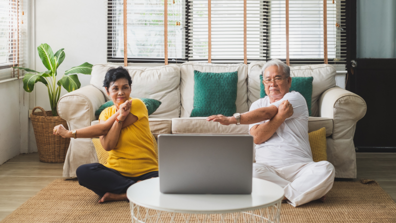 an older couple practices arm stretching while sitting on the floor