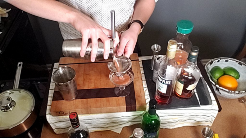 A mixologist measures liquor into a jigger.