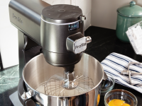 A dark grey GE Smart Stand Mixer sits on a grey counter with the whisk attachment and whipped egg whites inside the mixer bowl.