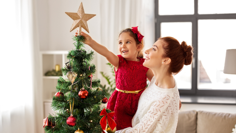 A child tops a Christmas tree with a gold star.