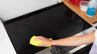 A person wipes a glass stove top with a rag.