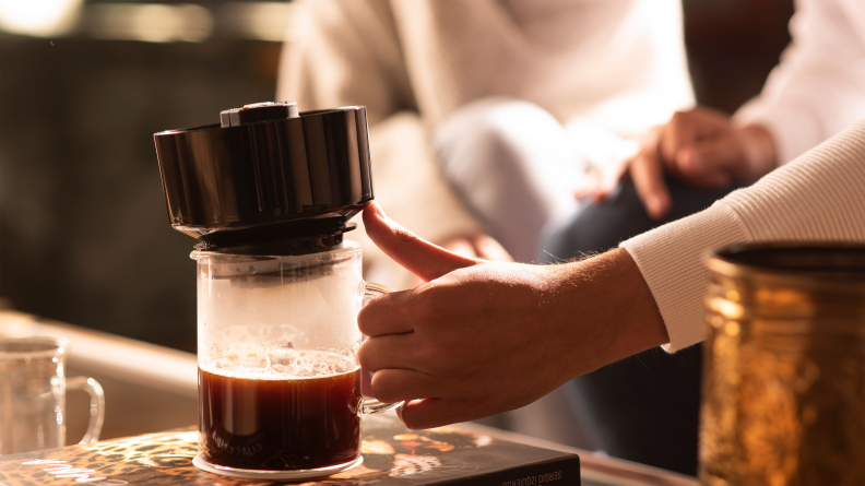 A person it lifting the top part of a VacOne coffee maker.