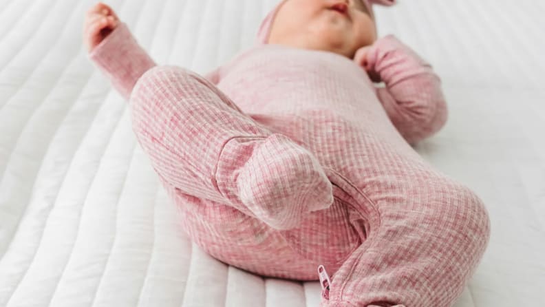 Close-up of a baby in pink footed pajamas lying on a white quilted bed.
