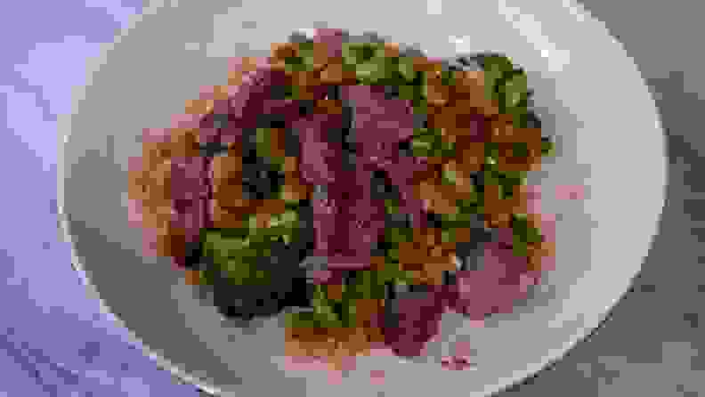 Cooked meat and vegetables inside of white bowl on countertop surface.