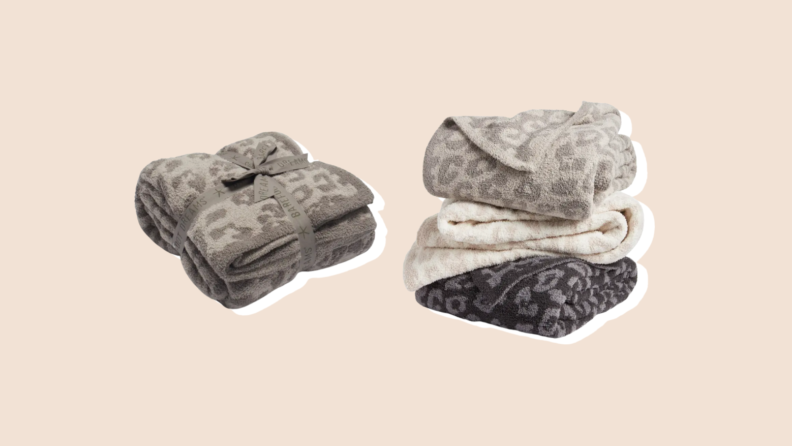 A wrapped gray-patterned Barefoot Dreams blanket sits next to a stack of three more, in gray, beige, and tone-on-tone black.