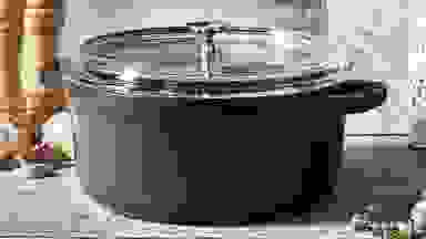 Black pot with clear glass lid on wooden countertop.
