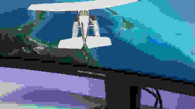 A plane flies over a bright blue lagoon on the screen of an ASRock Phantom Gaming PG34WQ15R2B monitor.