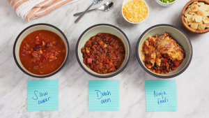 Three bowls of chili on a marble surface, labeled as "Slow cooker," "Dutch oven," and "Ninja Foodi"