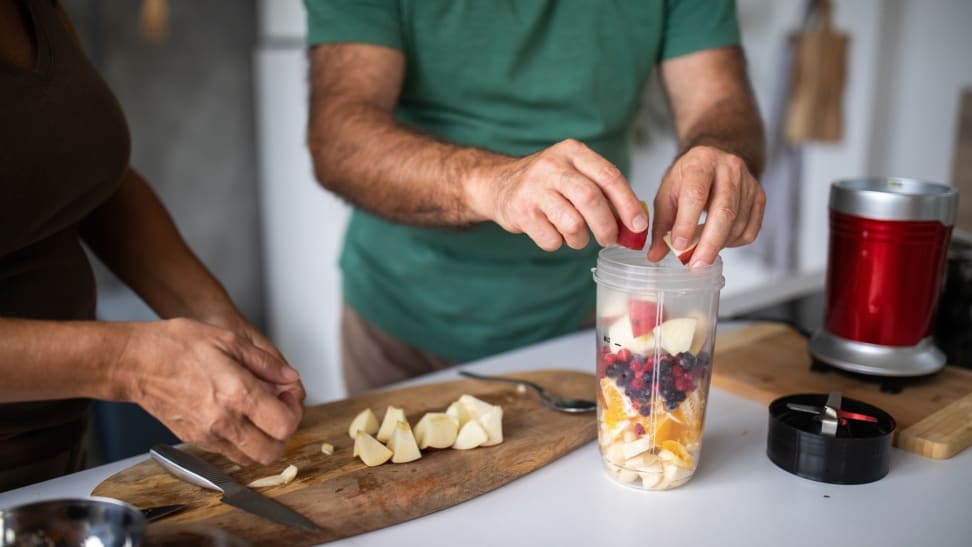 Two people chopping fruit and placing into a Magic Bullet blender for a smoothie