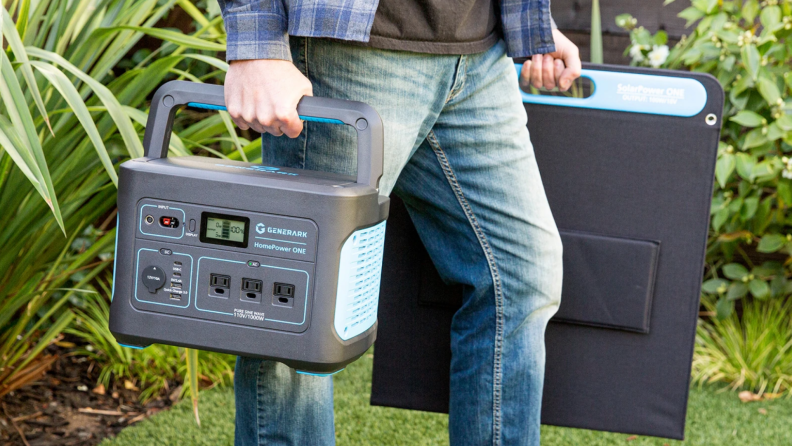 Person holding portable generator and solar panel outdoors.