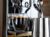 A close-up photo of the Breville Nespresso Creatista brewing an espresso shot and frothing milk.
