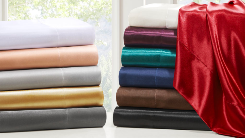 An image of the same set of satiny sheets in various different colors, folded and stacked together in two piles.