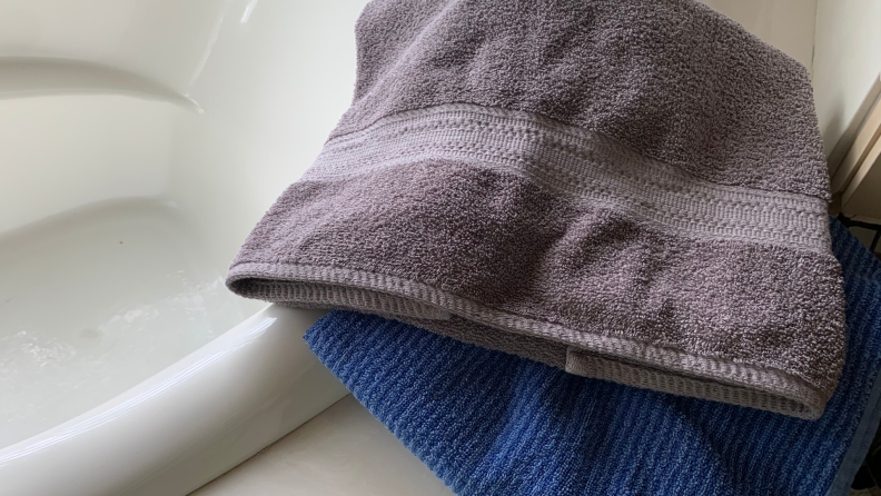 Gray and blue towel on top of the side of a white bathtub