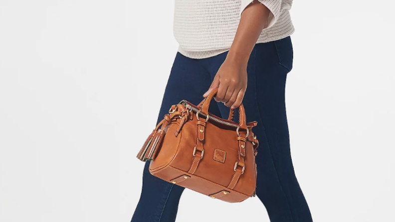 Woman carrying small brown leather Dooney & Bourke handbag.