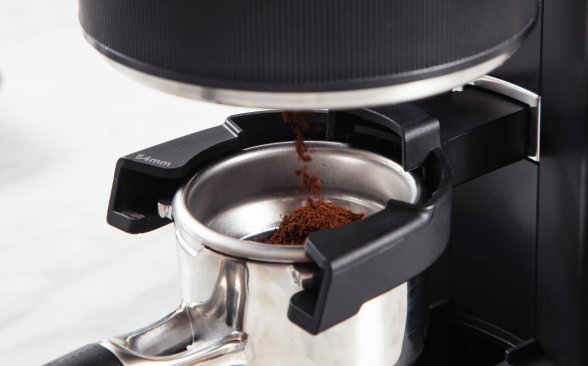 A close-up of a grinder ejecting coffee grounds into an espresso portafilter