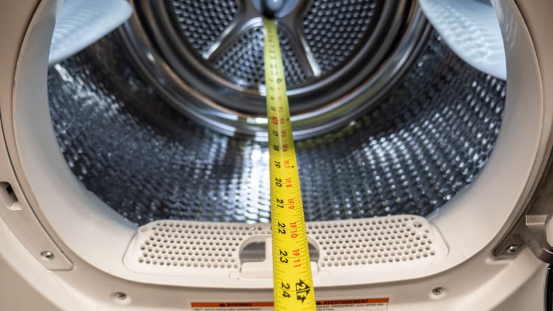 A yellow measuring tape stretches into the drum of a dryer showing it measures 24 inches