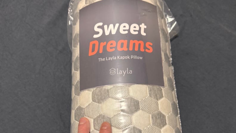 Layla Sleep Kapok Pillow shown rolled up in packaging against a dark grey background.