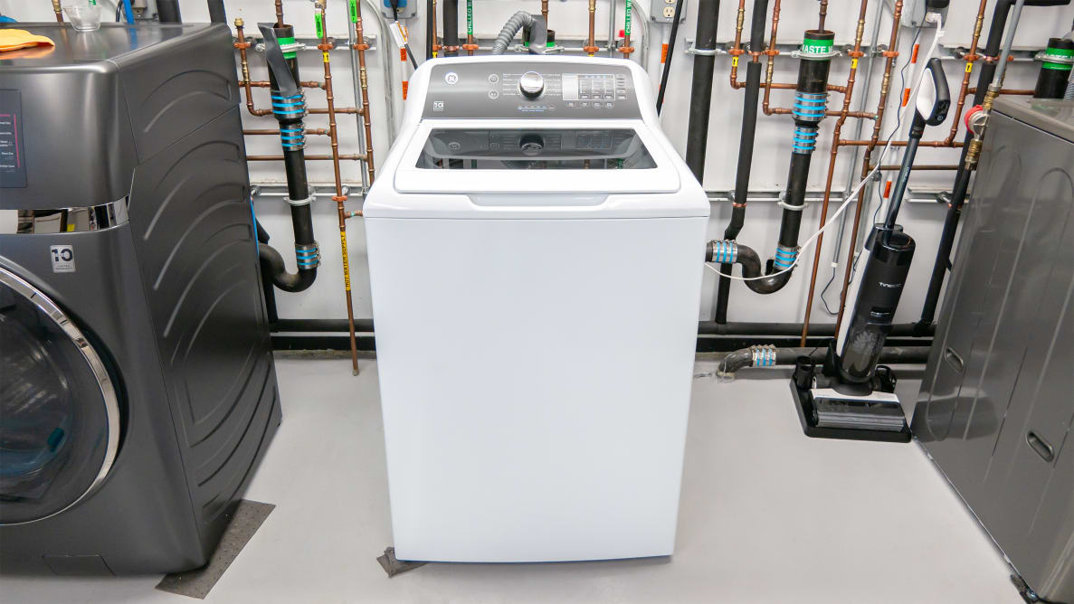 A solid white GE washer inside of the Reviewed testing labs in the middle of two other washing machine units.