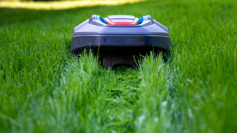A small robot lawn mower moving on a straight path through a grassy lawn.