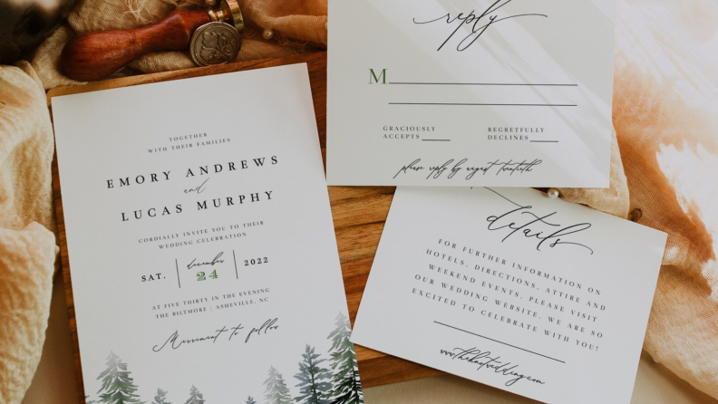 Set of three white wedding invitations with pine trees on front.