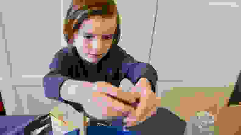 Young boy adding blue food coloring in blue bowl to slime.