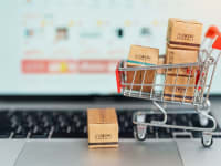 A miniature shopping cart sits on the keyboard of a laptop