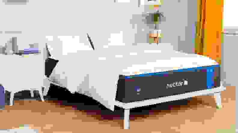 A Nectar mattress in a bedroom, covered with white bedding.