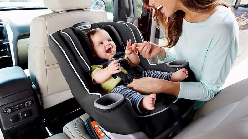 A smiling baby getting put into a carseat