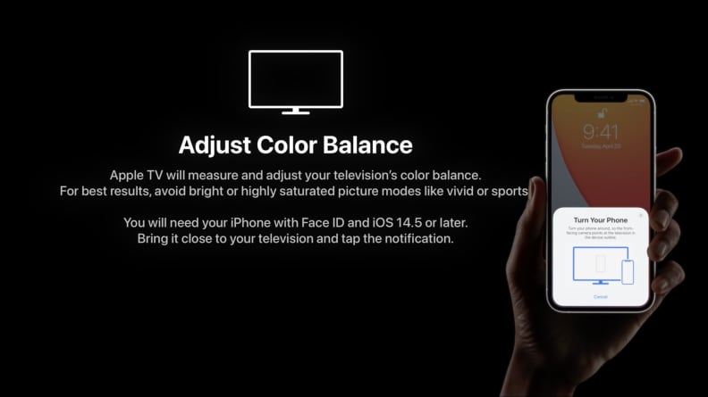 A person holds an iPhone to change the color correction on a darkened TV.