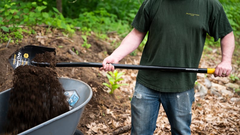 A person shoveling dirt into a wheelbarrow with a shovel