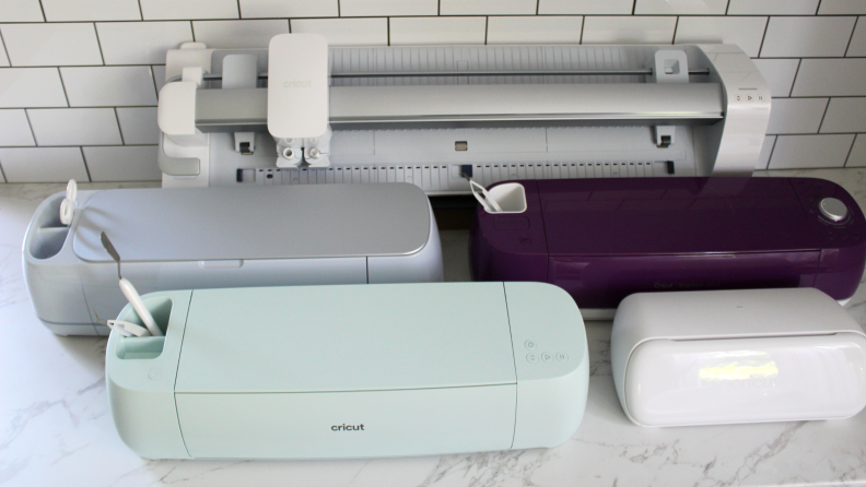 A group of variously colored Cricut machines assorted on a white countertop.
