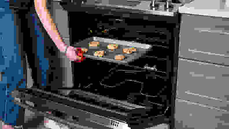 A person removes a tray of cookies from the oven using a red oven mitt.