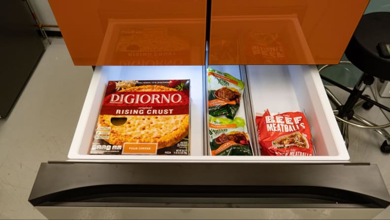 The bottom drawer of the fridge (freezer) opened showing some DiGiorno pizzas and beef.