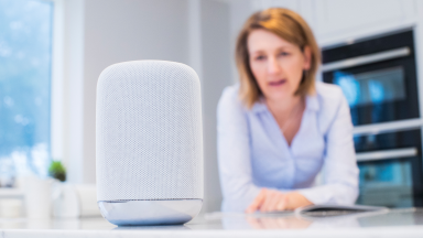 Person standing in kitchen talking to Amazon Alexa smart speaker.