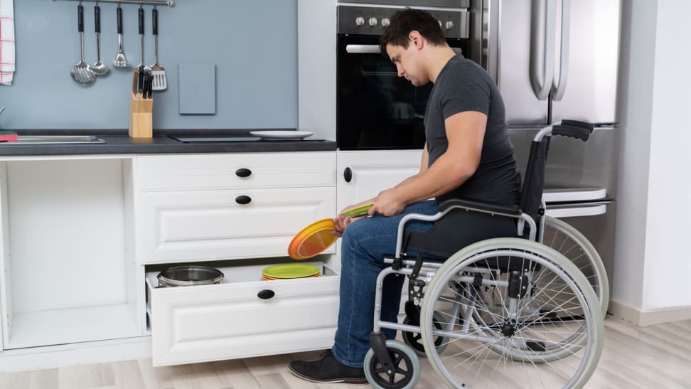 A man in a wheelchair puts away dishes in a kitchen.