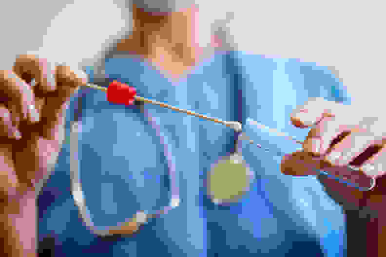 Close up of nurses hands holding buccal cotton swab and test tube ready to collect DNA from the cells.