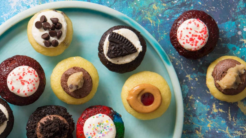 An image of several mini cupcakes in bright colors laid out on a blue plate and blue background.