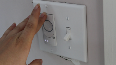 A person taps a smart switch for a ceiling fan and light inside a home.