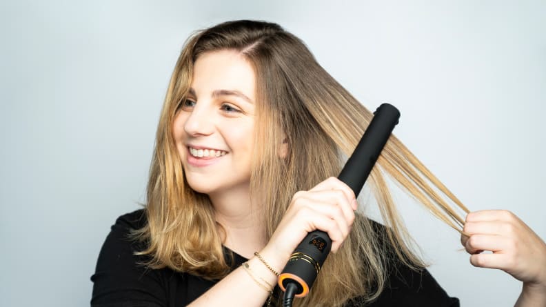 A woman using a hair straightener on her long hair.