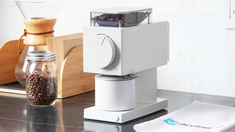 White Fellow Ode Gen 2 coffee grinder on countertop next to jar of coffee beans.