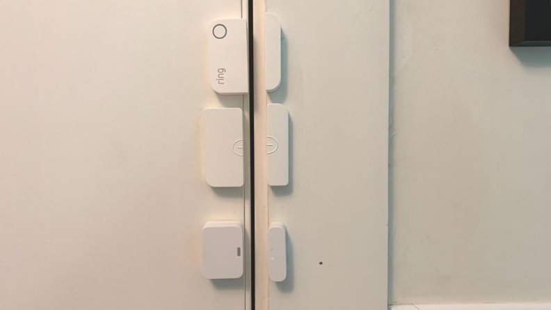 Three home security entry sensors are stuck to a white front door.