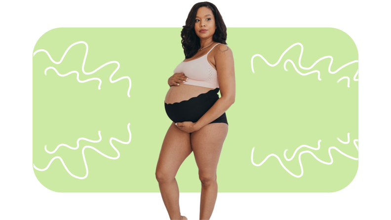 Pregnant model wearing light pink support bra top and solid black high rise underwear while holding baby bump.