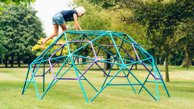 A child climbs up a Plum Play jungle gym outside.