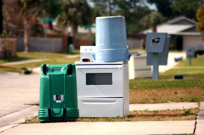 An old stove sits out on a curb along with other trash.
