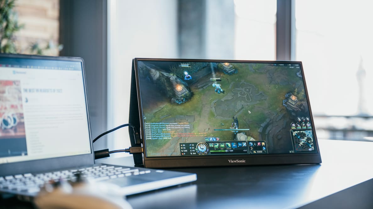 A small, portable gaming monitor standing upright on a desk with a controller attached