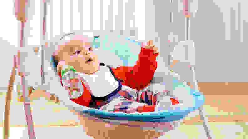 A child with a bottle and a bib sits in a blue baby swing.