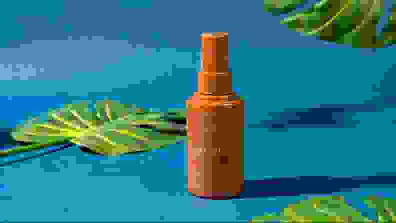 A bottle of face lotion against a blue background and foliage.