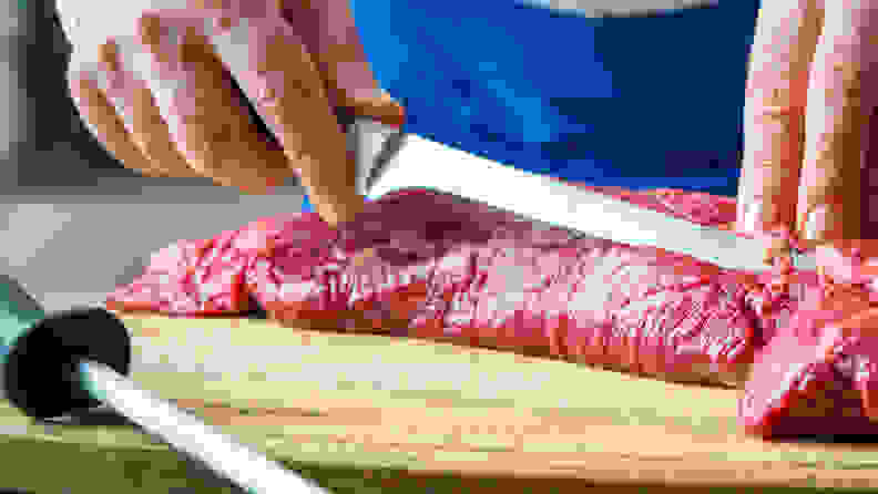 A person uses a knife to cut a large piece of meat.