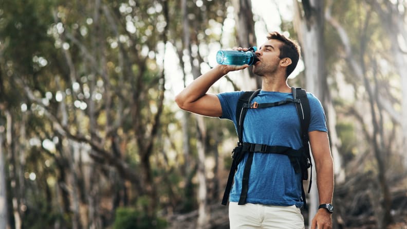 A man drinking from a water bottle on a hike.